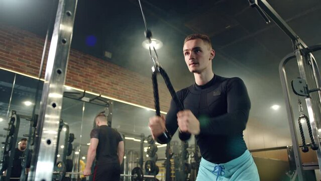 Young handsome man doing exercises on vertical row machine, hands, back workout. Sports facilities, man, woman exercising in gym in the background. High quality 4k footage
