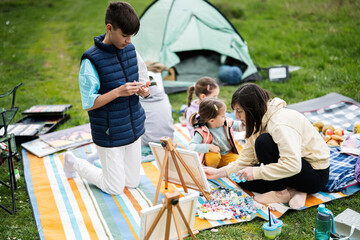 Happy young family, mother and children having fun and enjoying outdoor on picnic blanket painting at garden spring park, relaxation.