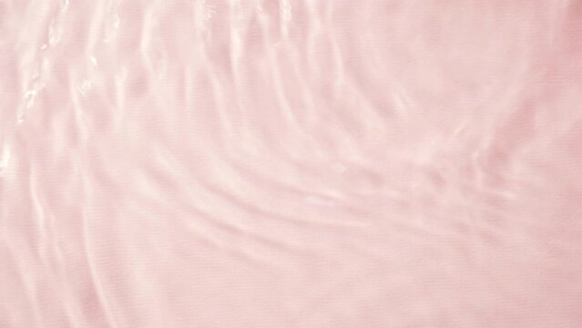Texture of a pink water surface with reflected, waves and ripples in sunlight