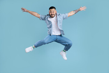 Fototapeta na wymiar Happy asian man wearing casual clothes, white shoes, stylish jeans jumping high isolated on blue background. Modern hipster listening music, positive lifestyle. Technology concept
