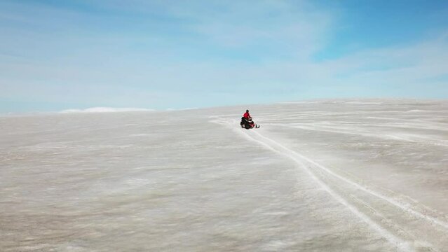Aerial view of a person doing stunts on a snowmobile, on the white surface of a glacier in Iceland, on a sunny day