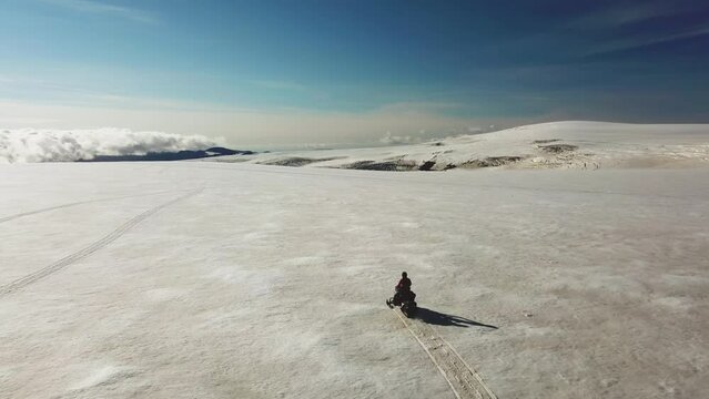 Aerial view of a person riding a snowmobile on a white glacier in Iceland, over the clouds, on a sunny day