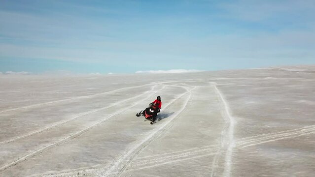 Aerial view of a person doing stunts on a snowmobile, on the surface of a glacier in Iceland, on a bright sunny day