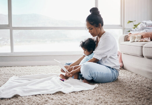 Time for cartoons. Full length shot of a young woman sitting in the living room with her daughter and using a digital tablet. - Powered by Adobe