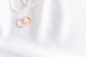 Two gold wedding rings on white satin textiles with pearl beads. Wedding festive background. A copy...