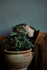 a young brown-haired man smelling his marijuana plant at home