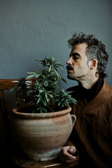 a young brown-haired man smelling his marijuana plant at home