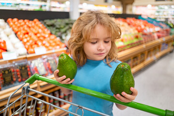 Portrait of child with shopping cart full of fresh vegetables in a food store. Supermarket shopping...