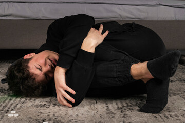 A severely depressed guy, lying on the floor among pills and a bottle of alcohol. A young man in a hard mental condition. alcohol and drugs addiction.