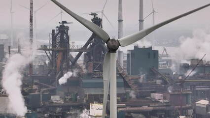 Close up orbiting view of a wind turbine in a dense industrial complex near the port of Port of Ijmuden Rotterdam, with the Tata Steel plant in the background