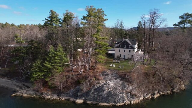 Orbit of evergreen trees and colonial home on a lakeside with blue skies and rolling hills in the background. Western Massachusetts, Berkshire county, New England, USA.
