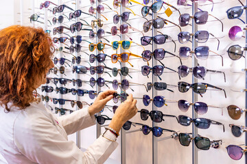 Sunglass Shopping: Red-haired Optometrist Trying on Trendy Eyewear in Front of Sunglass Display