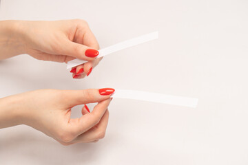 Woman hand with red nails with test strips for the perfume, isolated on a white background.