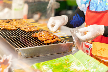 Woman grilling pork satay with chracoal.
