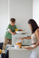 Woman preparing healthy meal with fruits and milk together with her little son