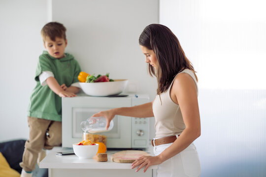 Woman preparing healthy meal with fruits and milk together with her little son