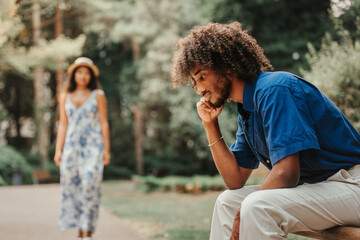 a black boy with Afro hair sitting in a garden. Pensive afro guy waiting for his girlfriend.