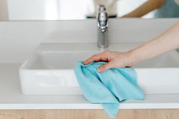 Woman hand cleaning washbasin with a blue cloth