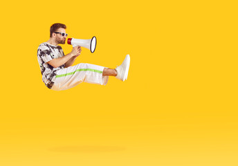 Portrait of a funny young bearded man wearing casual clothes holding mouthpiece on studio yellow background and jumping. Guy shouting and screaming announcement in megaphone. Advertising concept.