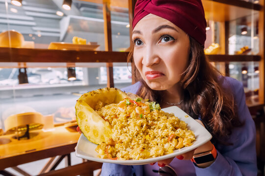 A woman dissatisfied customer of the thai restaurant sniffs the disgusting smell of a pineapple rice dish with spoiled ingredients and is going to complain to the chef