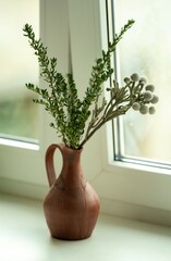 green decorative branches in a clay jug on the windowsill