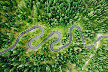 Cars on driveway of famous Snake Road surrounded by forests and meadows. Serpentine Snake Road across Giau Pass surrounded by mountain ranges in summer forest