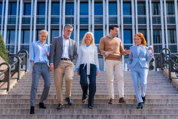 Obraz premium Cheerful group of coworkers outdoors in a corporate office area walking down some stairs going to work, middle-aged businesswoman and businessman