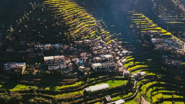 4k, Aerial view of Rural terrace farming on a hilly landscape and Himalayan village (Jhalpari) of Uttarakhand, India, with mud Houses and cow shelters on a hilltop. Drone view of dense Forest