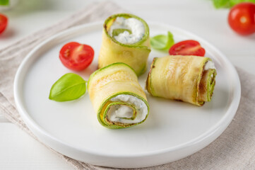 Zucchini appetizer rolls with cream cheese, garlic and herbs on a plate on a white wooden background. Selective focus.