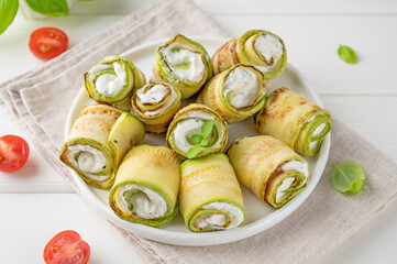 Zucchini appetizer rolls with cream cheese, garlic and herbs on a plate on a white wooden background. Selective focus.