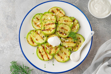Slices of fried zucchini with garlic and fresh dill on a plate on a gray concrete background. Vegetarian healthy dish. Selective focus.