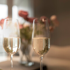 Two glasses of champagne with defocused flowers in the background and softly illuminated windows