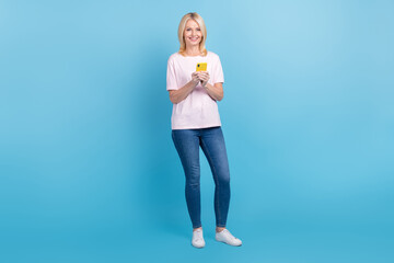 Full length photo of cheerful person dressed white t-shirt denim pants read notification on smartphone isolated on blue color background