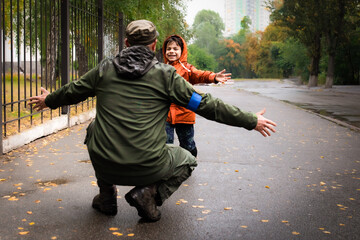 Military man in olive uniform and cap meeting his son outdoors in summer rainy day