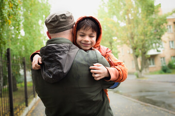 Military man in olive uniform and cap hugging his little son after long parting