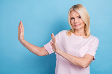 Photo of serious focused aged lady arms palms show block stop gesture empty space isolated on blue...