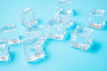 Ice cubes with water drops scattered on a blue background, top view.
