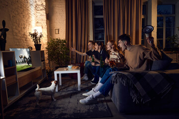 Naklejka na ściany i meble Group of friends, sport fans sitting on couch at home in the evening and emotionally watching online football match. Concept of friendship, leisure activity, weekends, fun, emotions