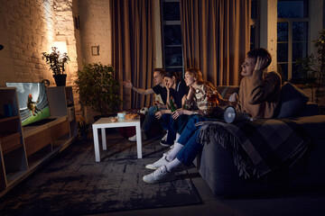 Loosing game. Group of friends sitting on couch at home in the evening, emotionally watching live...