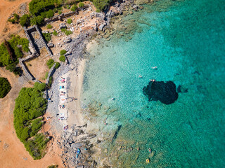 Top down aerial view of tourists on a small beach with crystal clear blue ocean on the island of Crete, Greece