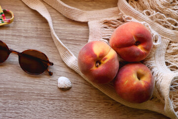 Floral yellow bikini, wicker bag, retro sunglasses, seashell, bag with peaches and cut watermelon on wooden background. Top view, copy space.