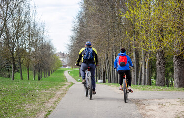 Senior man and woman are exercising on bicycles outdoors, they are a couple. Back view .