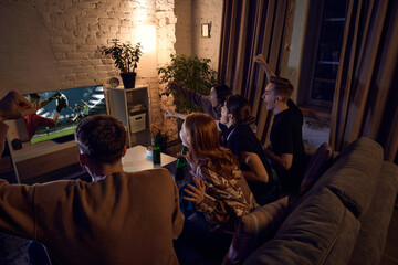 Group of friends watching live american football translation, cheering up team and drinking beer at...