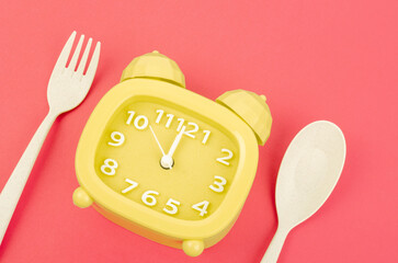 The Yellow alarm clock with cutlery on red color background. Concept of intermittent fasting, lunchtime, diet and weight loss