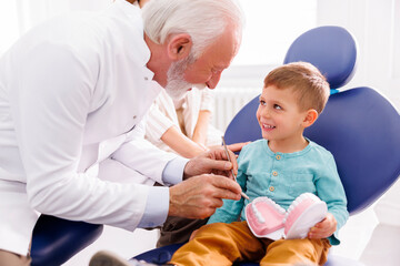 Dentist showing checkup procedure on plastic jaw model to child patient