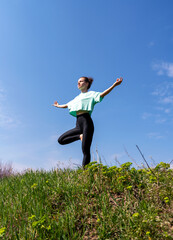 Woman stands on hill in yoga pose against blue sky and meditating.