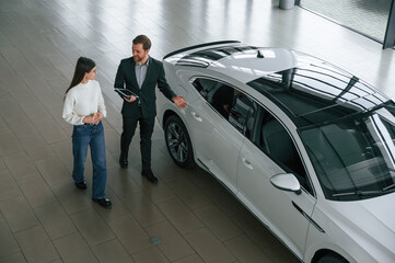 Talking, holding tablet. Man is showing the new automobile to the woman customer in the car...