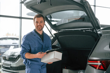 With box and notepad. Man in blue uniform is working in the car service