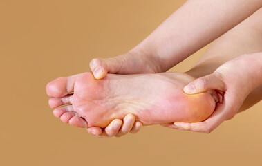 Woman with severe plantar pain is massaging her foot, isolated on beige background