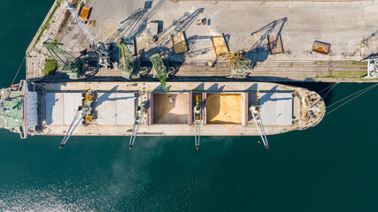 Loading dry cargo ship of wheat by cranes in port. Top down view loading into holds of sea cargo vessel